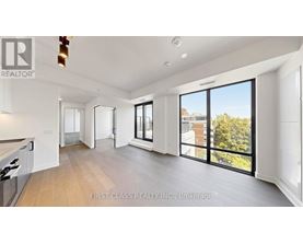 A spacious, well-lit living room with a kitchen area and sliding glass doors.