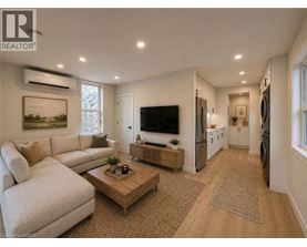 A well-lit living room with a white sofa, a wooden coffee table, and a flat-screen TV mounted on the wall.