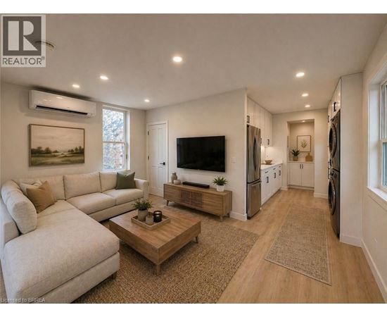 A well-lit living room with a white sofa, a wooden coffee table, and a flat-screen TV mounted on the wall.