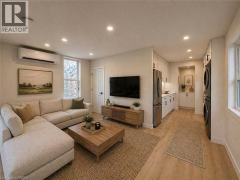 A well-lit living room with a white sofa, a wooden coffee table, and a flat-screen TV mounted on the wall.