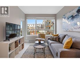 A living room with a grey couch, a black coffee table, a television, and a large window with a view of a building.