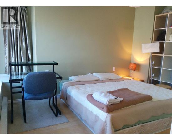 A bedroom with a bed, chair, and nightstand.