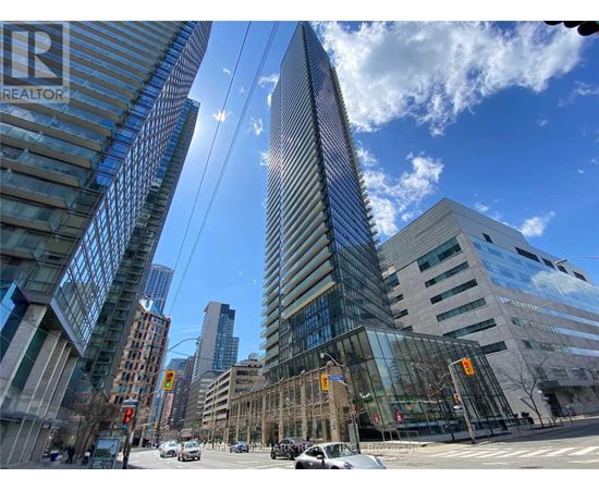 A tall glass building stands in the middle of a city intersection.