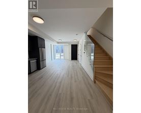 A spacious room with wooden flooring and a staircase on the right side.