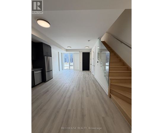A spacious room with wooden flooring and a staircase on the right side.