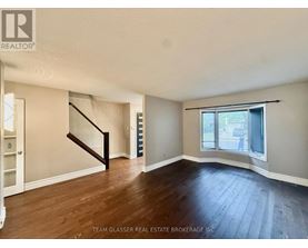 A room with wooden floors and a staircase leading to another room.