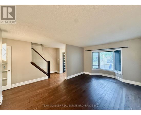 A room with wooden floors and a staircase leading to another room.