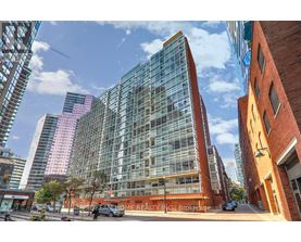 A modern glass building stands in front of a row of brick buildings.
