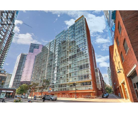 A modern glass building stands in front of a row of brick buildings.