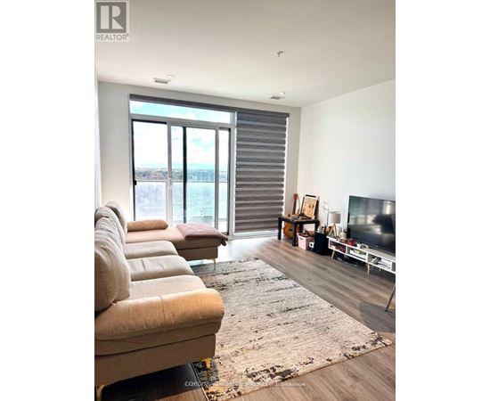 A living room with a couch, a rug, a television, and a window with blinds.