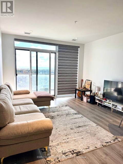 A living room with a couch, a rug, a television, and a window with blinds.