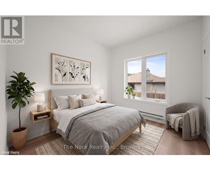 A bedroom with a large bed, a potted plant, and a window overlooking a house.