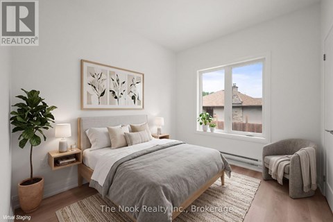 A bedroom with a large bed, a potted plant, and a window overlooking a house.