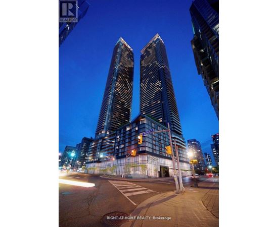 Two tall buildings are shown at night with a street in front of them.