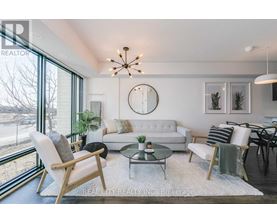 A well-lit living room with a white couch, a glass coffee table, and a large window.