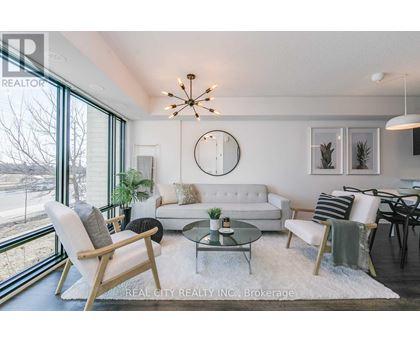 A well-lit living room with a white couch, a glass coffee table, and a large window.