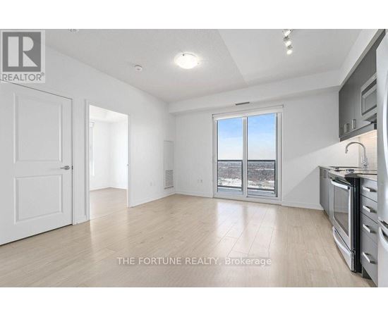 A well-lit, empty room with a kitchen area to the right and a door to the left.