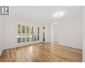 A spacious room with wooden flooring and a large window with blinds.