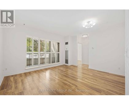 A spacious room with wooden flooring and a large window with blinds.