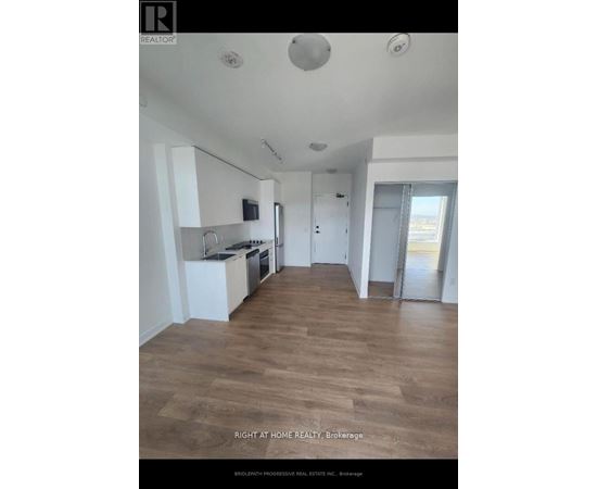 A spacious kitchen with wooden flooring and white walls.