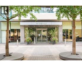 A realtor sign is on the left side of a building with a glass entrance.
