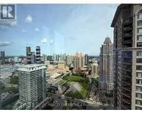 A cityscape with a mix of modern and older buildings, a clear sky, and a green park area in the foreground.
