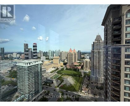 A cityscape with a mix of modern and older buildings, a clear sky, and a green park area in the foreground.