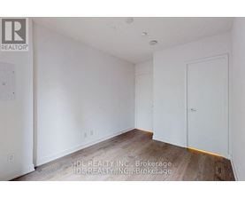 A room with white walls and wooden flooring, with a door on the right side.