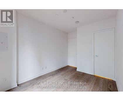 A room with white walls and wooden flooring, with a door on the right side.