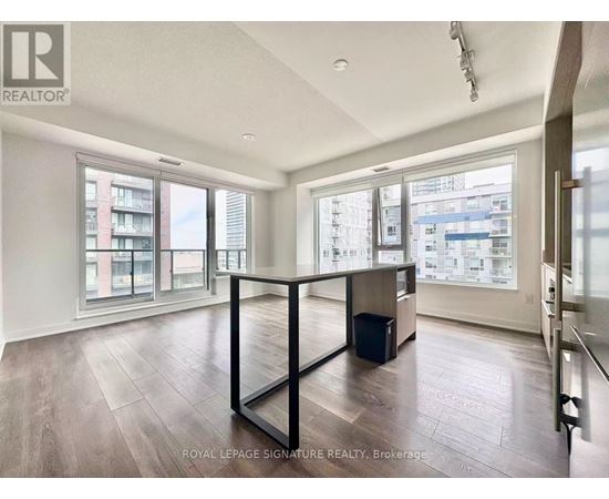 A spacious room with wooden flooring and large windows overlooking a cityscape.