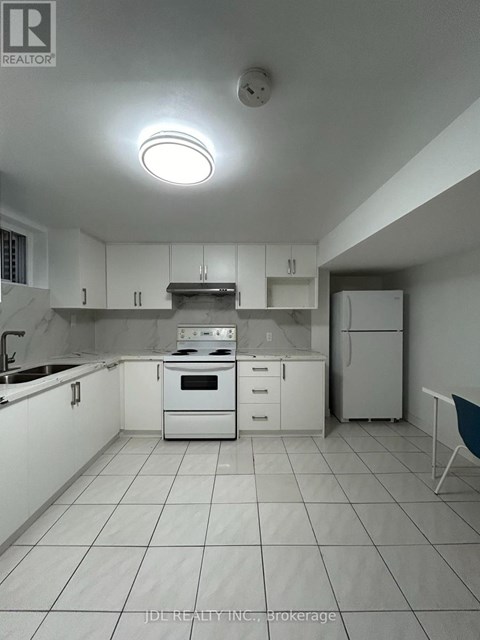 A white kitchen with a stove top oven and a refrigerator.