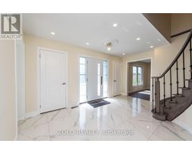 A spacious hallway with marble flooring and a staircase with black railings.
