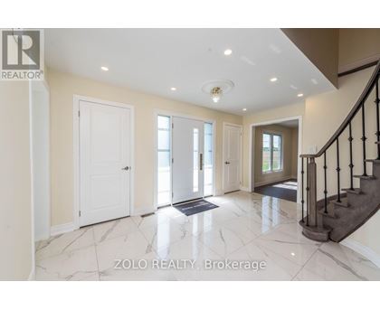A spacious hallway with marble flooring and a staircase with black railings.