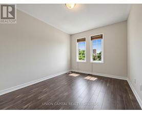 A room with wooden floors and two windows showing a view of a building and trees.