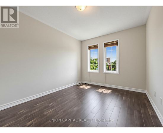 A room with wooden floors and two windows showing a view of a building and trees.