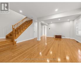 A spacious room with wooden flooring and a staircase.