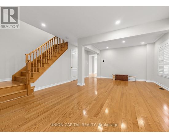 A spacious room with wooden flooring and a staircase.
