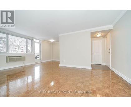 A spacious room with wooden flooring and white walls, with a doorway leading to another room.