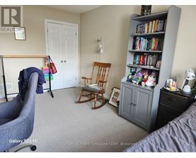 A bedroom with a grey armchair, a wooden rocking chair, a bookshelf filled with books, and a white door.