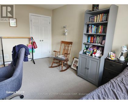 A bedroom with a grey armchair, a wooden rocking chair, a bookshelf filled with books, and a white door.