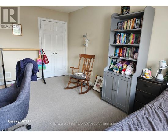 A bedroom with a grey armchair, a wooden rocking chair, a bookshelf filled with books, and a white door.