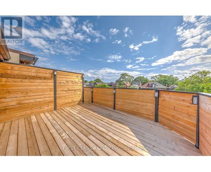 A wooden deck with a railing and a view of the sky and trees.