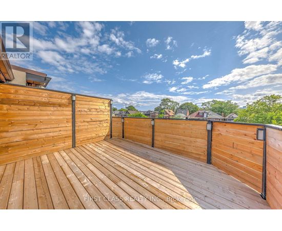 A wooden deck with a railing and a view of the sky and trees.