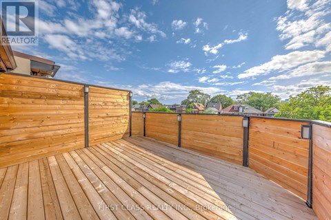 A wooden deck with a railing and a view of the sky and trees.