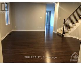 A spacious room with wood flooring and a staircase on the right side.