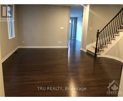 A spacious room with wood flooring and a staircase on the right side.