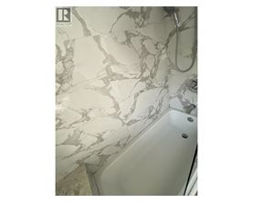 A white bathtub with a marble patterned wall behind it.