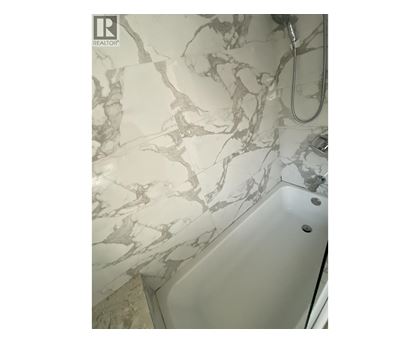 A white bathtub with a marble patterned wall behind it.