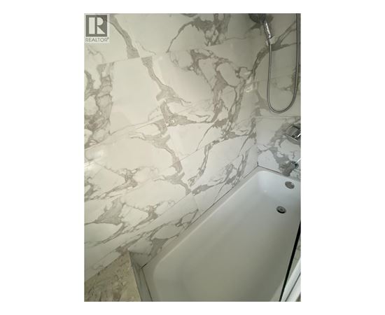 A white bathtub with a marble patterned wall behind it.