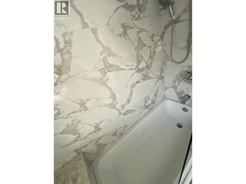 A white bathtub with a marble patterned wall behind it.